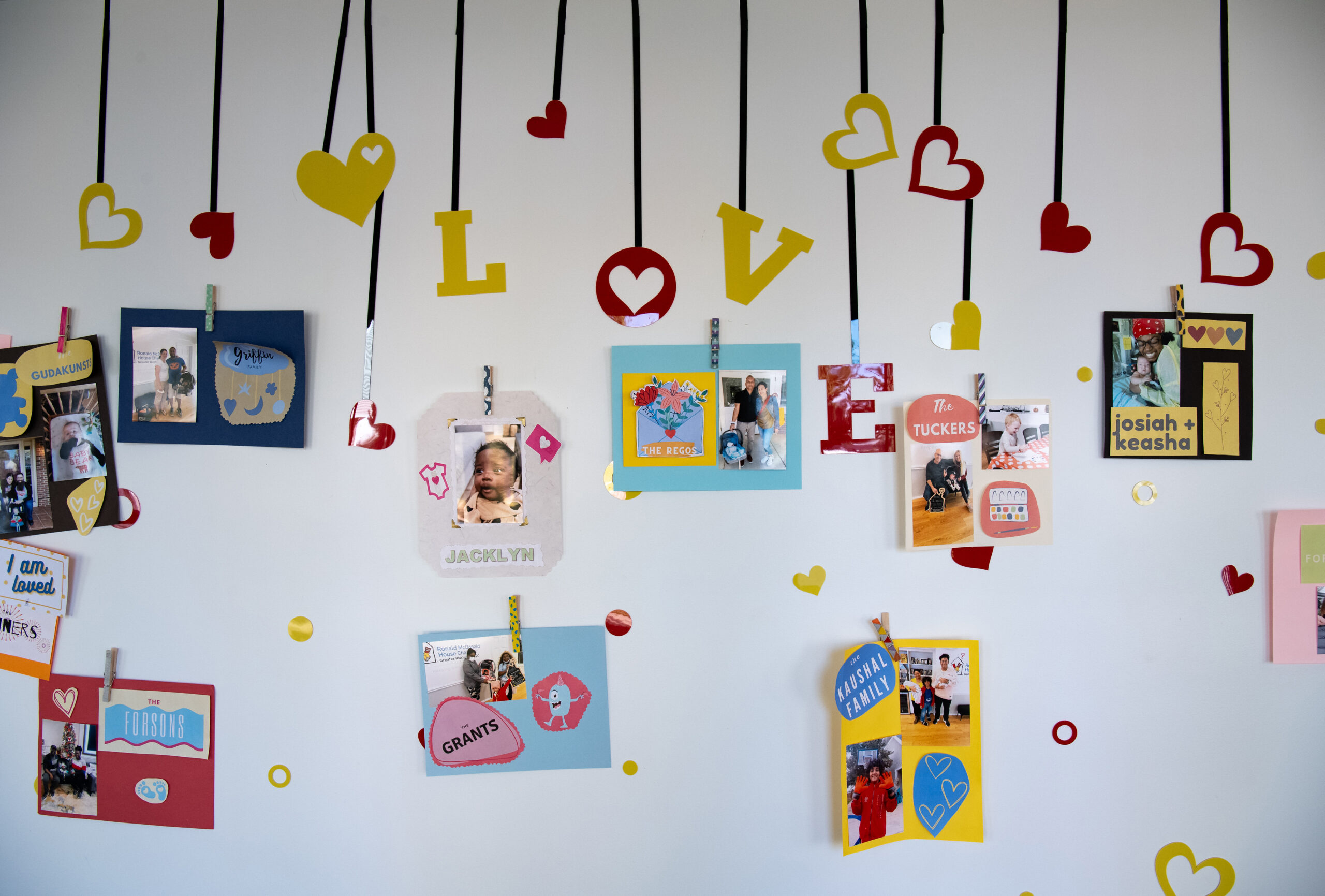 A wall adorned with colorful cards and photos clipped on black ribbons. The decorations include hearts and the word 